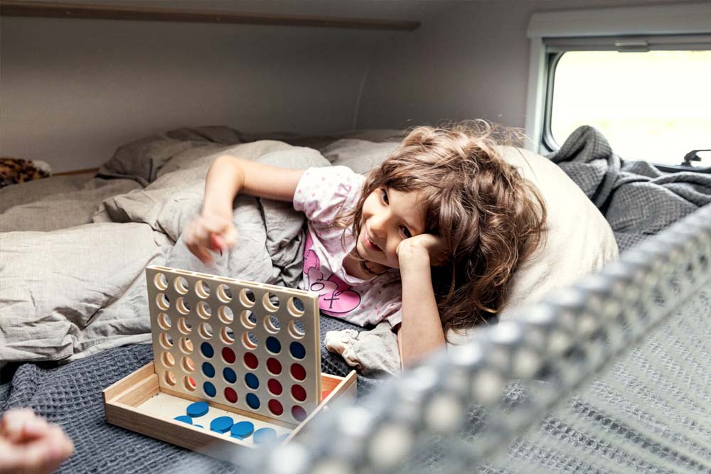 Kind spielt sicher im Bett von Alkoven mit den Bettenmassen 1,60 x 2.10 Meter, ein Netz schützt das Kind, damit dieses nicht aus dem Bett des teilintegrierten Wohnmobils fallen kann