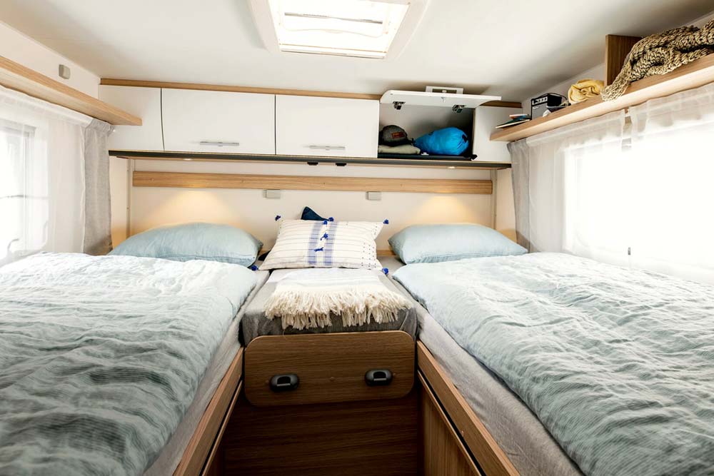 Gemütliches großes Längsbett mit blauem Bettbezug und zusammensteckbaren Mittelteil im Wohnmobil von Roadfans. Die Bettenmasse betragen 200 / 195 x 194 cm