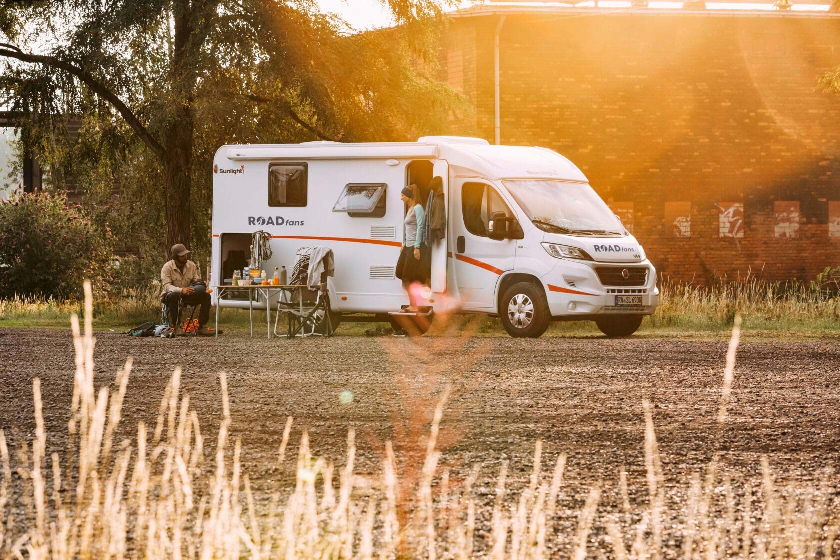 Zwei Personen sind im Wohnmobilurlaub und campen mit einem teilintegrierten Wohnmobil names Freedom auf einem Feld und essen an einem Campingtisch