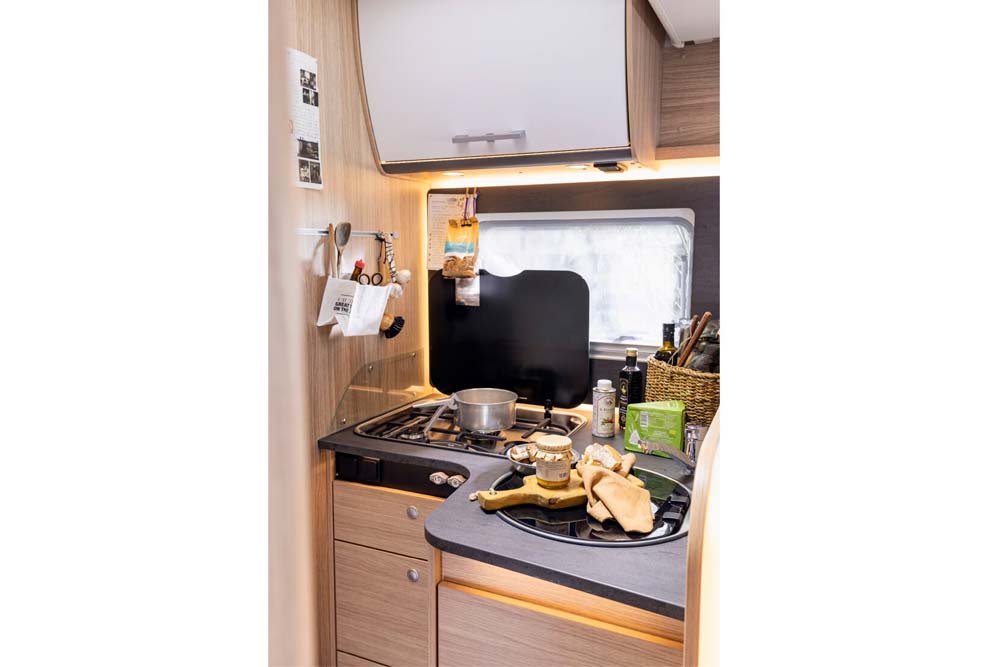 Große Küche mit drei Gasherdplatten und einem Spülbecken mit Geschirr in einem vollintegrierten Wohnmobil namens Independence von Roadfans