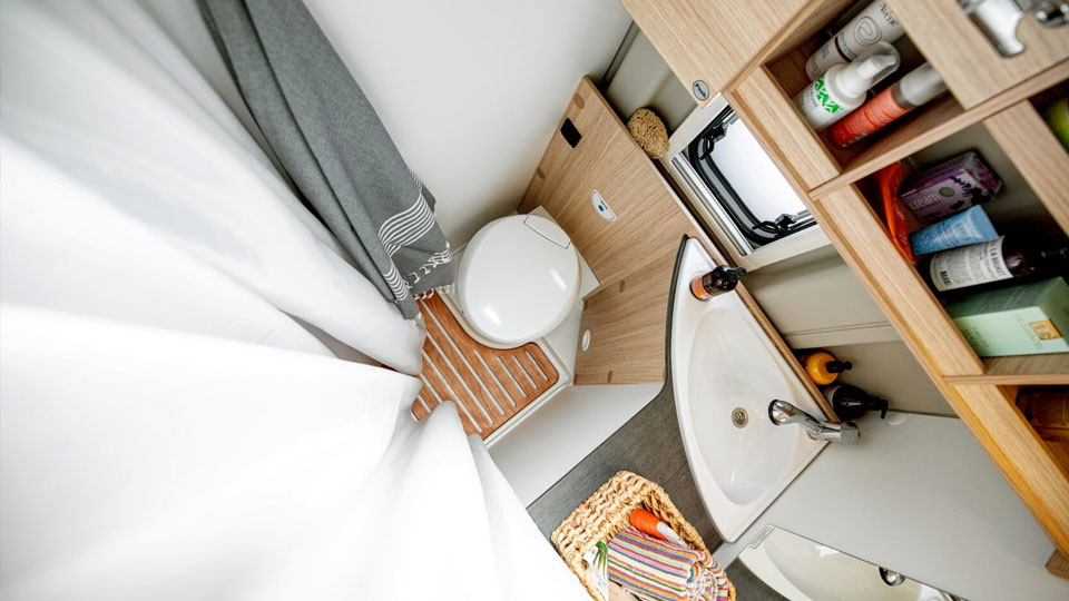 Geschlossener weißer Duschvorhang und WC mit Waschbecken im Badezimmer von Wohnmobil Kastenwagen Journey 4 von Roadfans