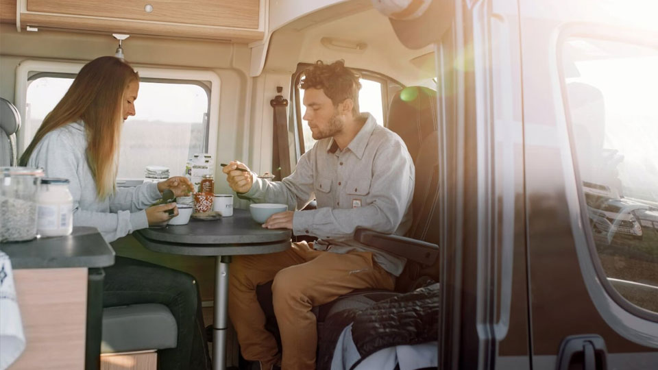 Ein junges Paar frühstückt bei Sonnenschein in einem Wohnmobil Kastenwagen von Roadfans