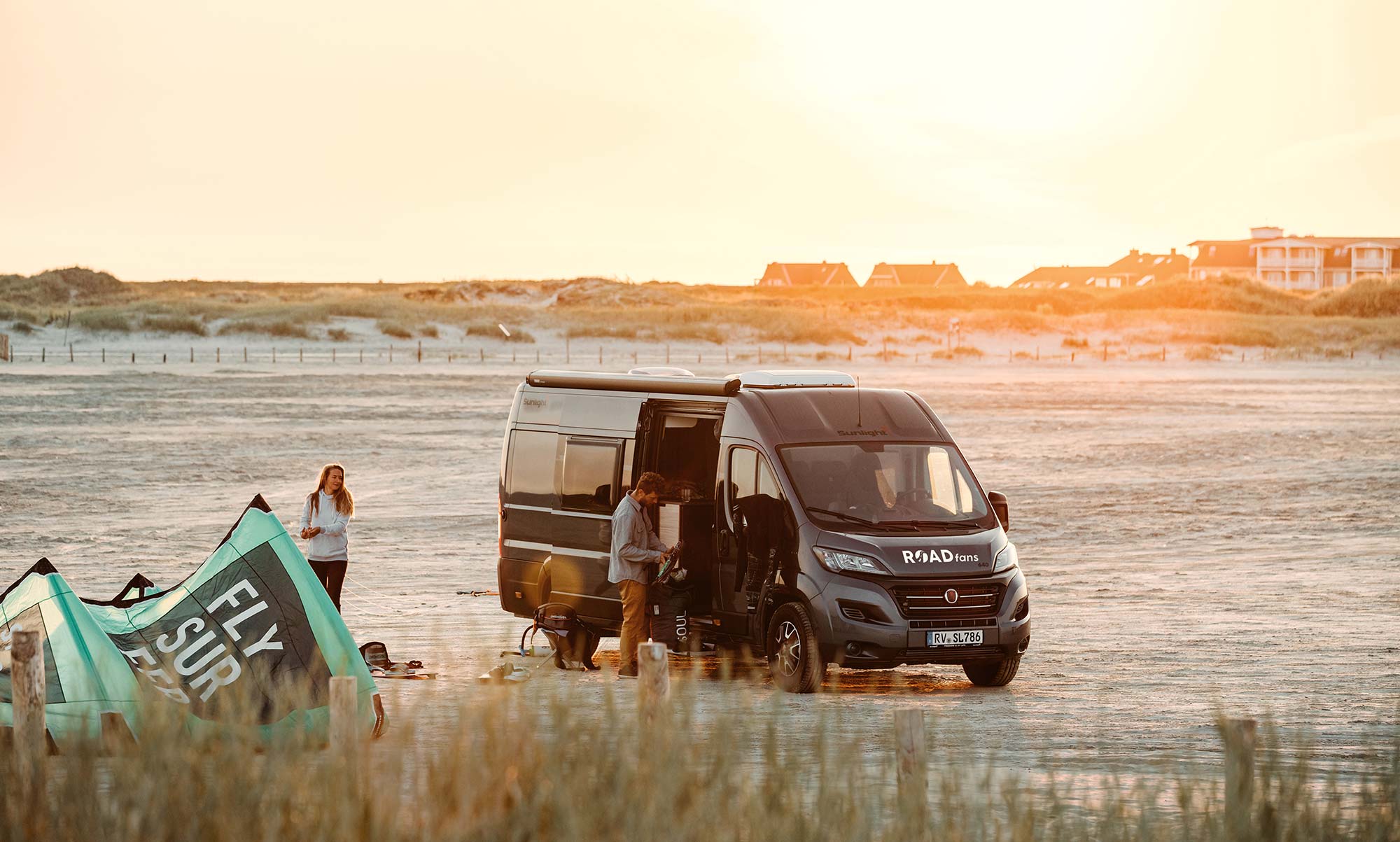 Kastenwagen Journey Plus von Roadfans steht am Strand im Sonnenuntergang mit einem jungen Paar.