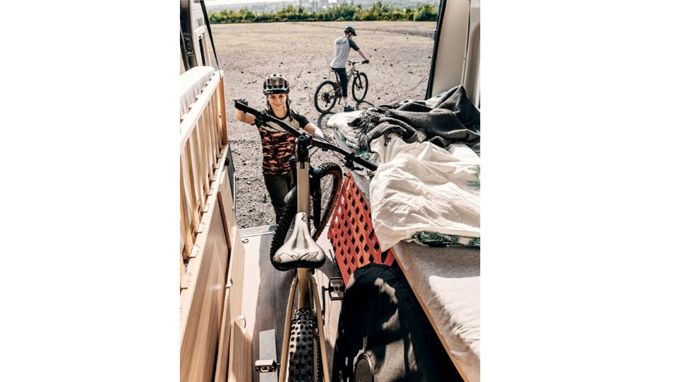Frau hebt Fahrrad aus Heckgarage von Kastenwagen Journey