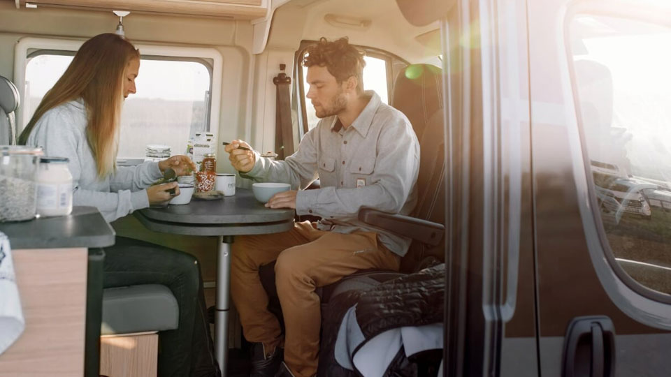Im morgendlichen Sonnenschein frühstückt ein junges Paar in der Sitzecke im Wohnmobil Kastenwagen Journey
