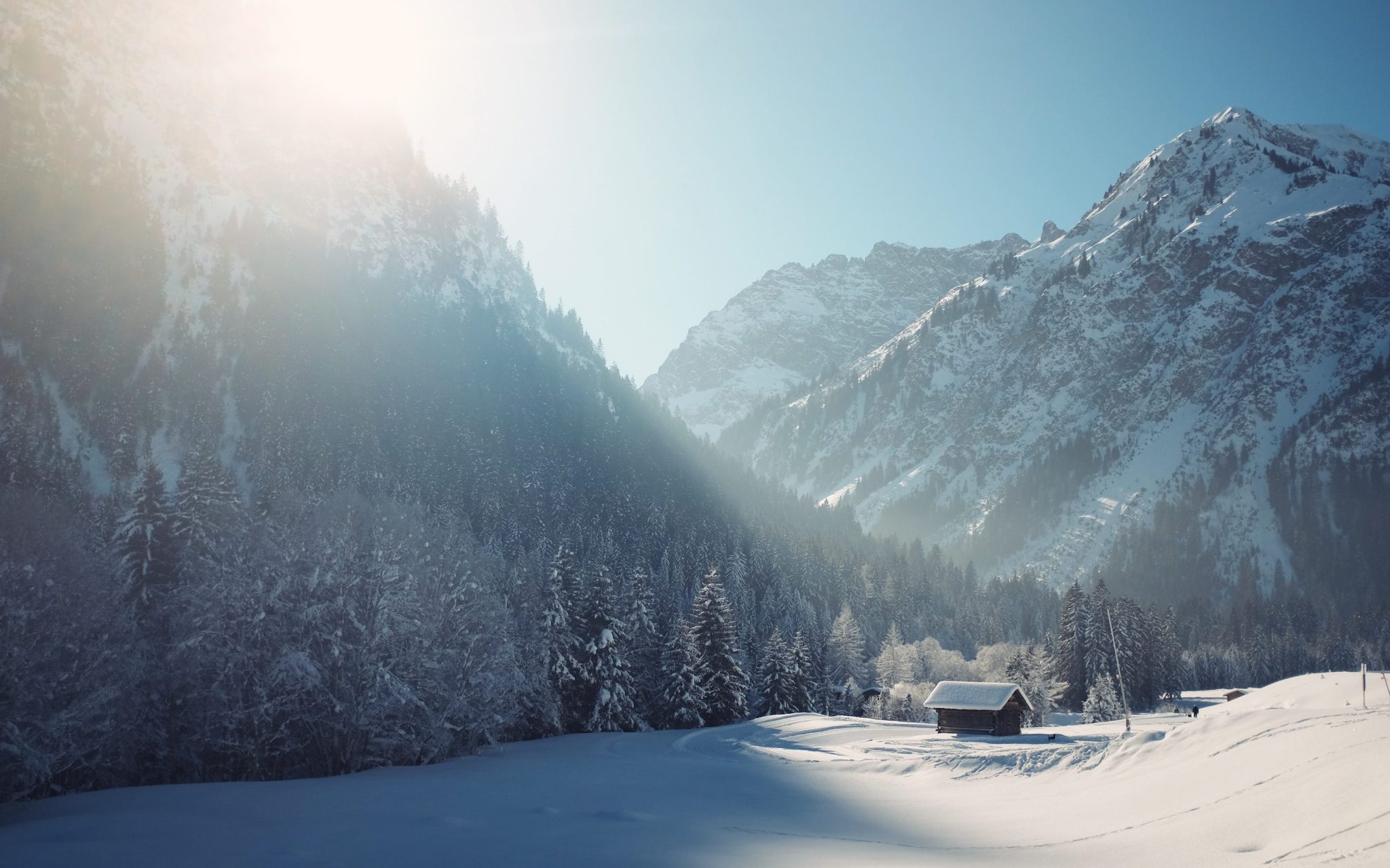 Winterlandschaft mit Bergen, Bäumen und eine kleine Hütte in der Ferne