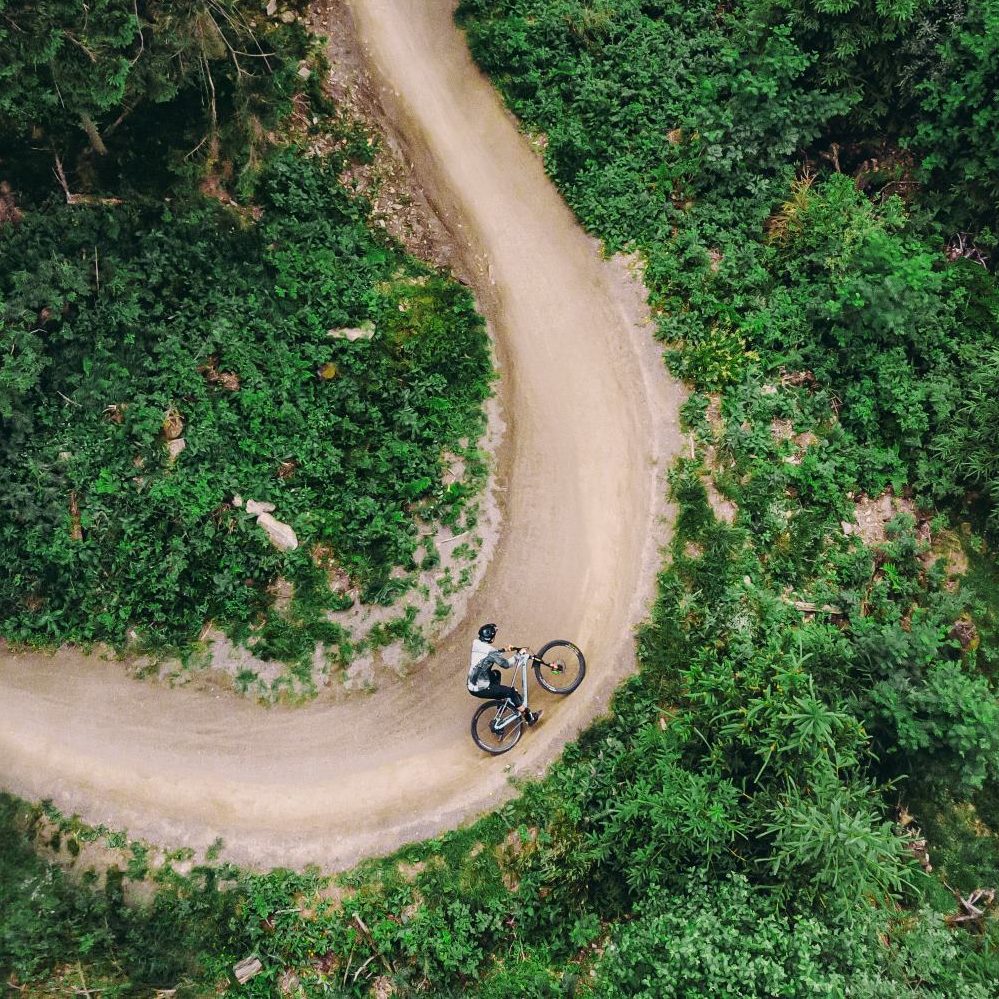 Fahrradfahrer auf einer kurvigen Strecke im Wald aus der Vogelperspektive fotografiert