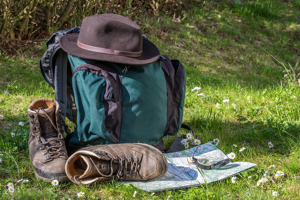 Packliste Wanderurlaub - Blick auf einen Wander- rucksack, -schuhe, -karte, Hut und Kompass auf einer Wiese.