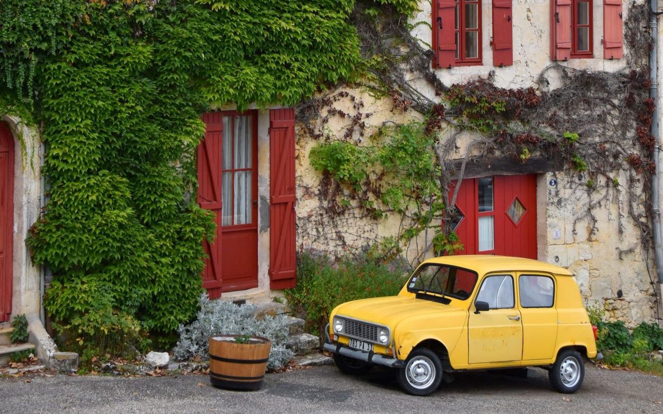 Kleines gelbes und altes Auto vor einer Hauswand mit Wein berankt