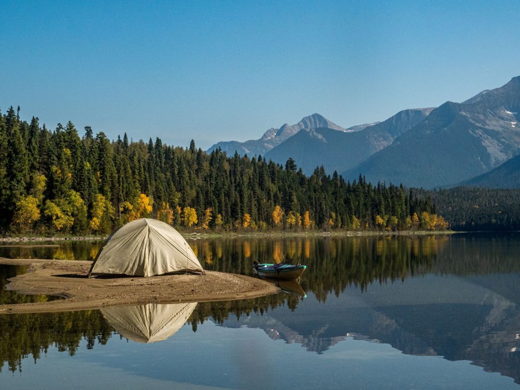 Nachhaltig Campen - Blick auf einen Wald, einen See sowie Berge im Hintergrund. Im Vordergrund steht ein Zelt und ein kleines Boot im See.