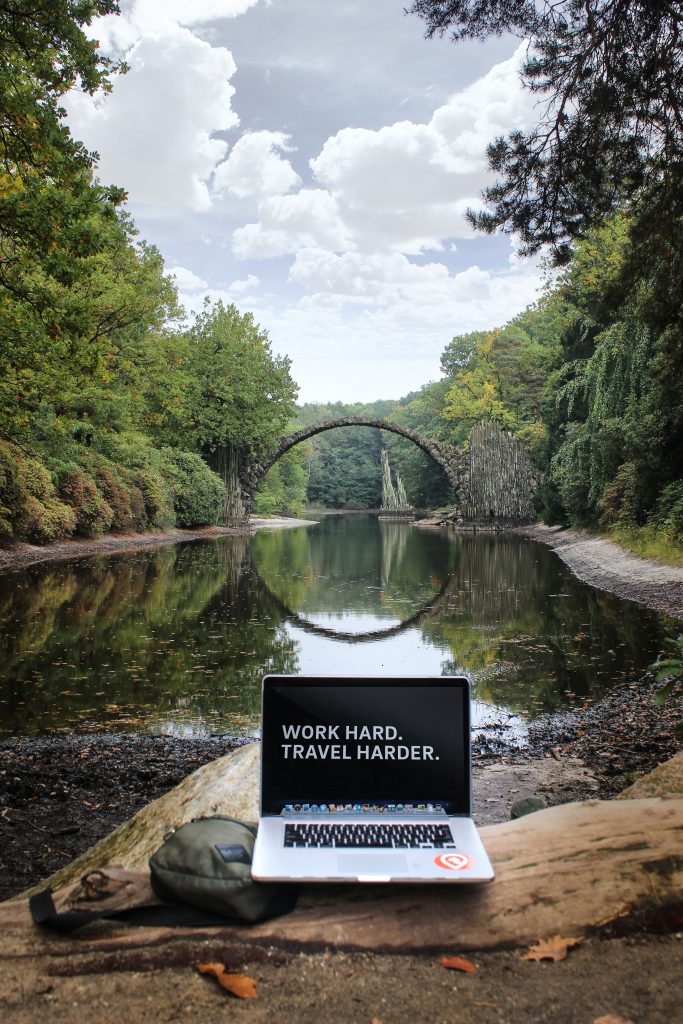 Bester WLAN-Router für Wohnmobil - Laptop in der Natur mit einer alten Brücke über einen urigen Fluss im Hintergrund 