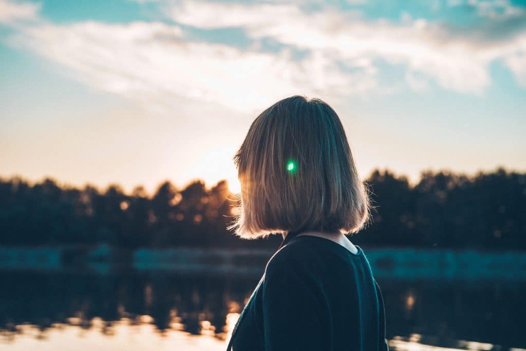 Camping Sauerland - Frau im Vordergrund blickt auf einen See und Bäume im Sonnenuntergang 