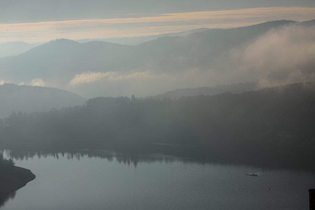 Camping Sauerland - Blick über den See auf einen Wald im Nebel