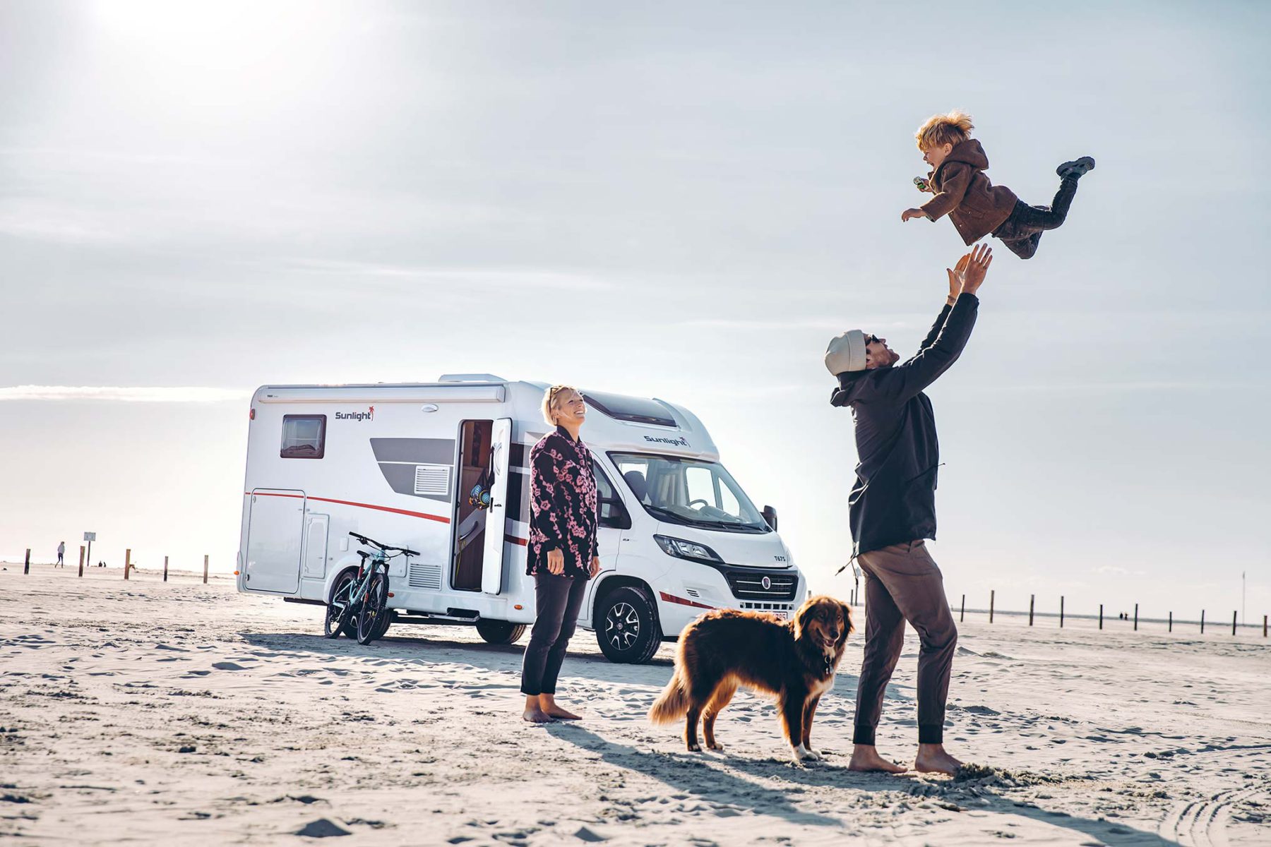 Familie am Strand mit Hund im Hintergrund steht ein Wohnmobil