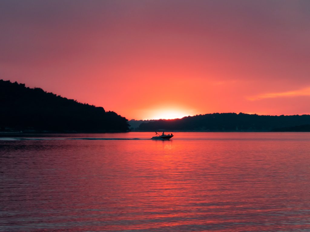 Glamping Kroatien - Sonnenuntergang mit einem kleinen Schlauchboot auf dem Wasser im Vordergrund 