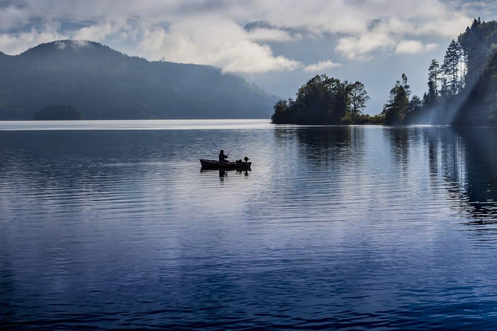 Camping Angeln direkt am Wasser - Blick auf eine Person, die im Boot sitzt und angelt.