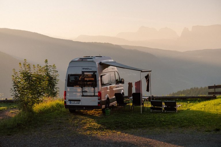 Ganzjahres-Campingplatz - Wohnmobil mit ausgefahrener Sonnenmarkise auf einer Wiese bei Dämmerung