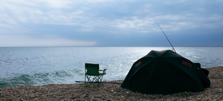 Camping Angeln direkt am Wasser - Blick auf ein kleines Zelt, in dem jemand am Wasser am angeln ist.