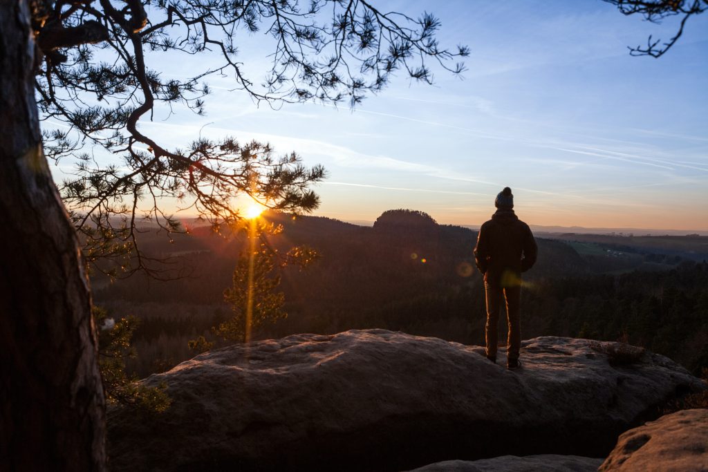 Camping Sächsische Schweiz - Mann steht auf einem Fels und guckt den Sonnenuntergang über dem Wald