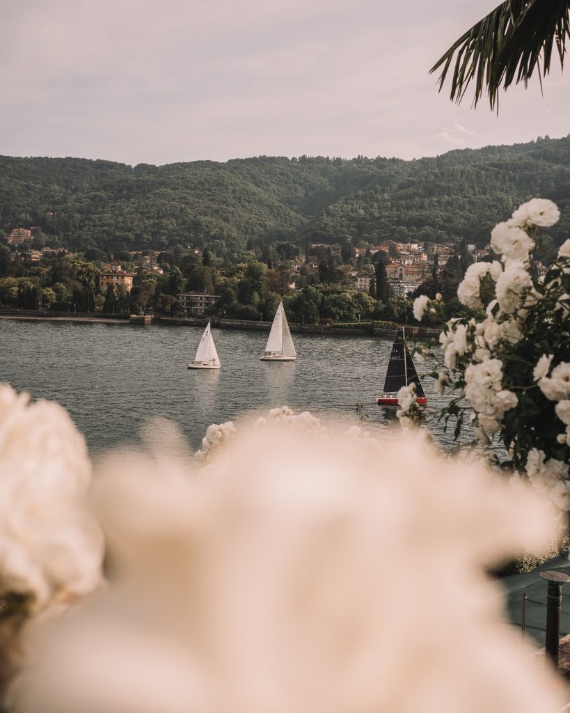 Camping Lago Maggiore mit Hund - Blick über unscharfe Blumen auf den See mit Segelbooten darauf. 