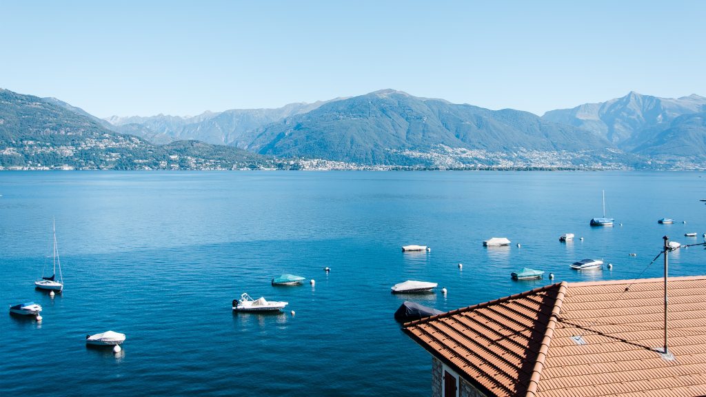 Camping Lago Maggiore mit Hund - Der See mit bewaldeten Bergen im Hintergrund. Auf dem See sind kleinen Motorboote 