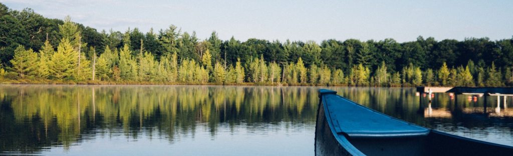 See mit Kanu und einem Wald im Hintergrund