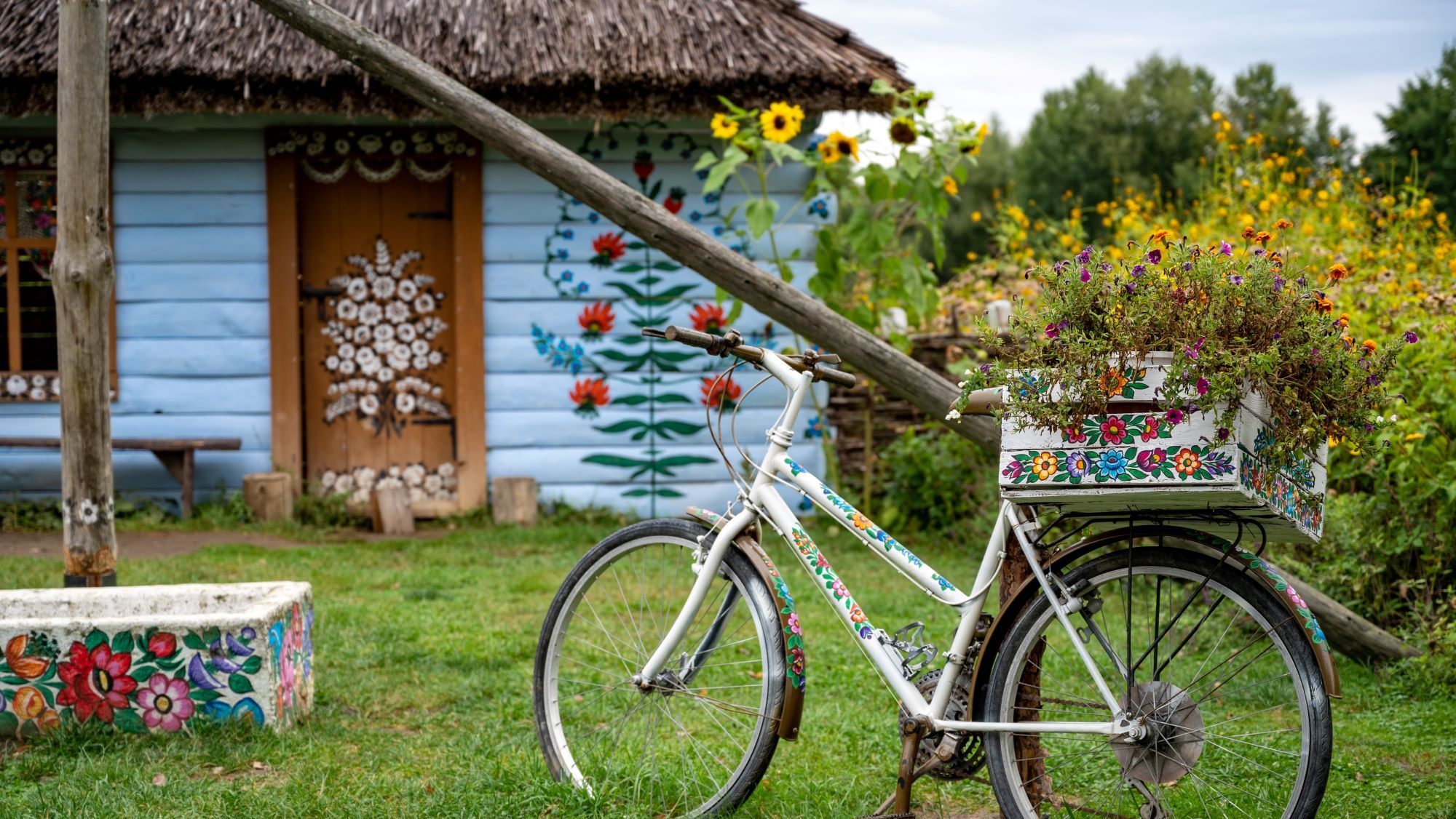 Fahrrad mit Korb mit Blümchen bemalt im Hintergrund ein blaues Haus mit Blümchen auf der Fassade