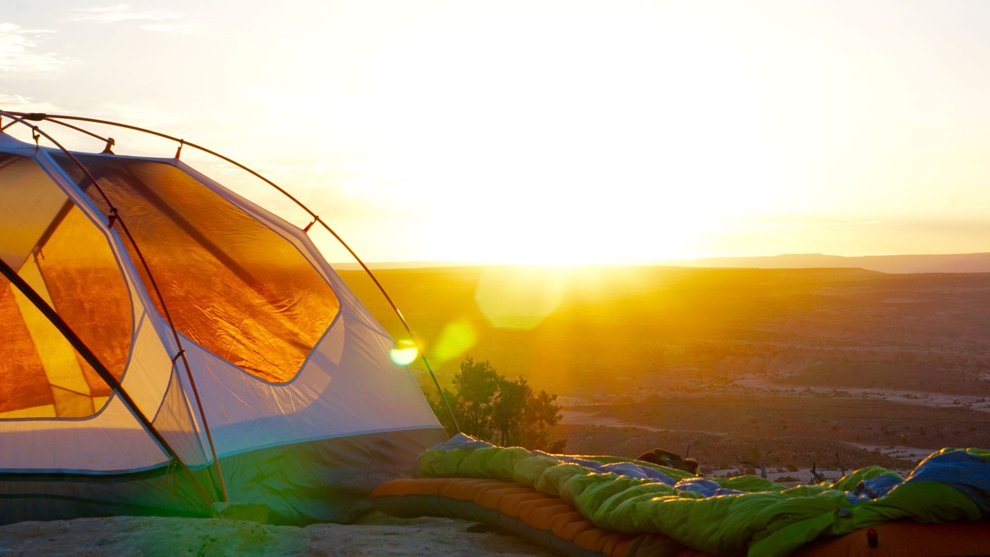 Camping für Anfänger - Zelt und Schlafsack bei Sonnenaufgang an einer Klippe